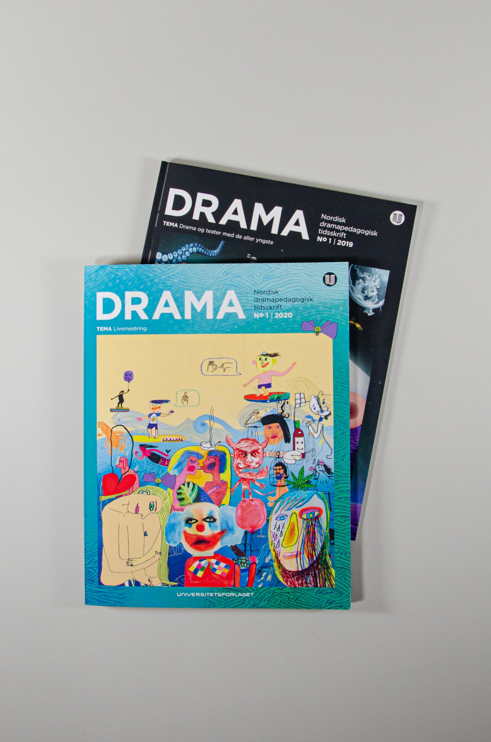 Bildet viser to utgaver av Drama som ligger oppå hverandre.